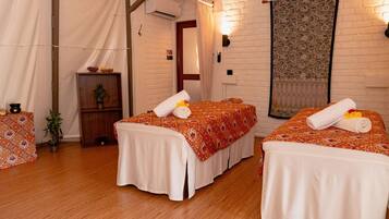 Two single beds with white linens and orange bedspreads, a potted plant, and a small cabinet.