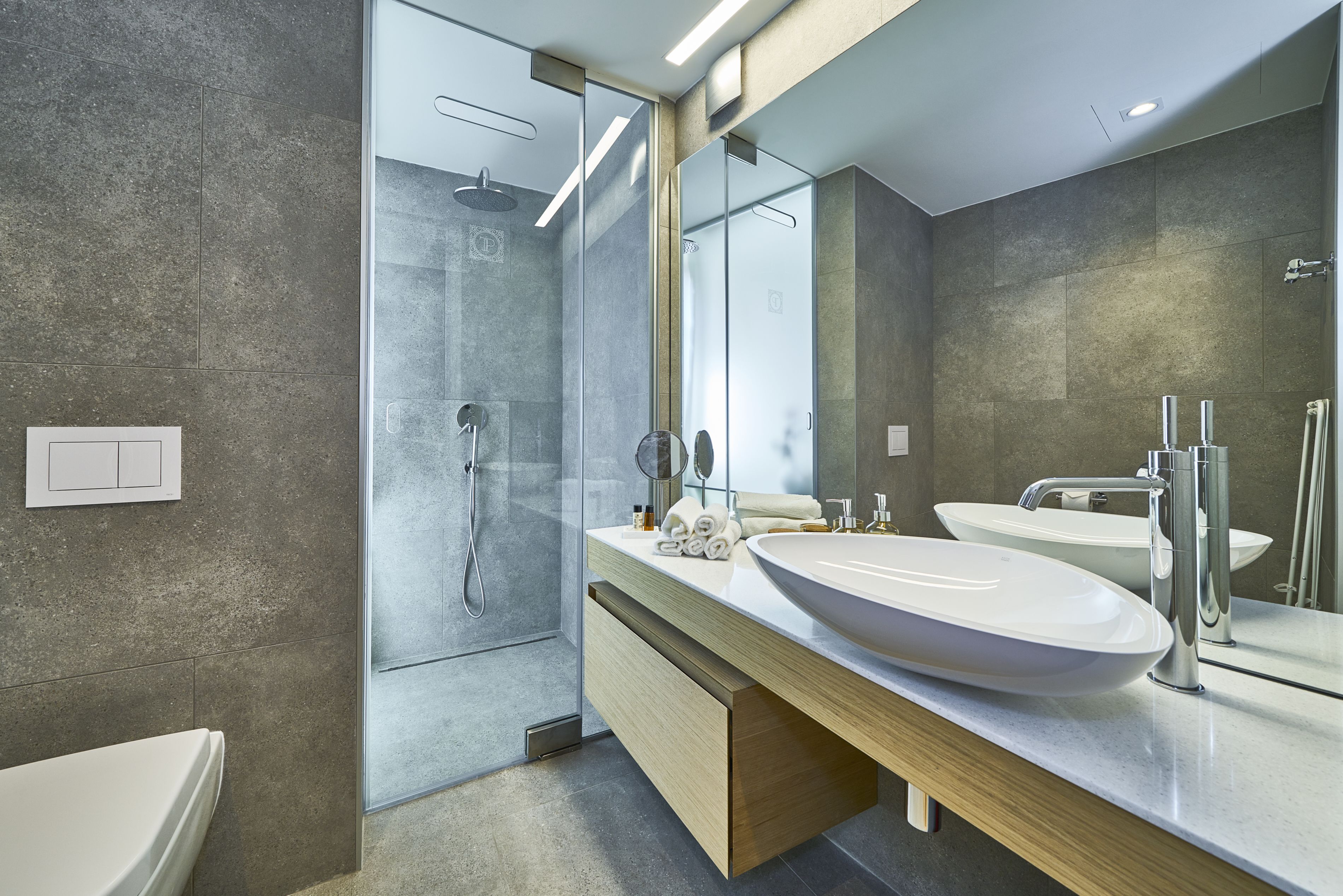 A modern bathroom with a large mirror, two sinks, and a shower area.