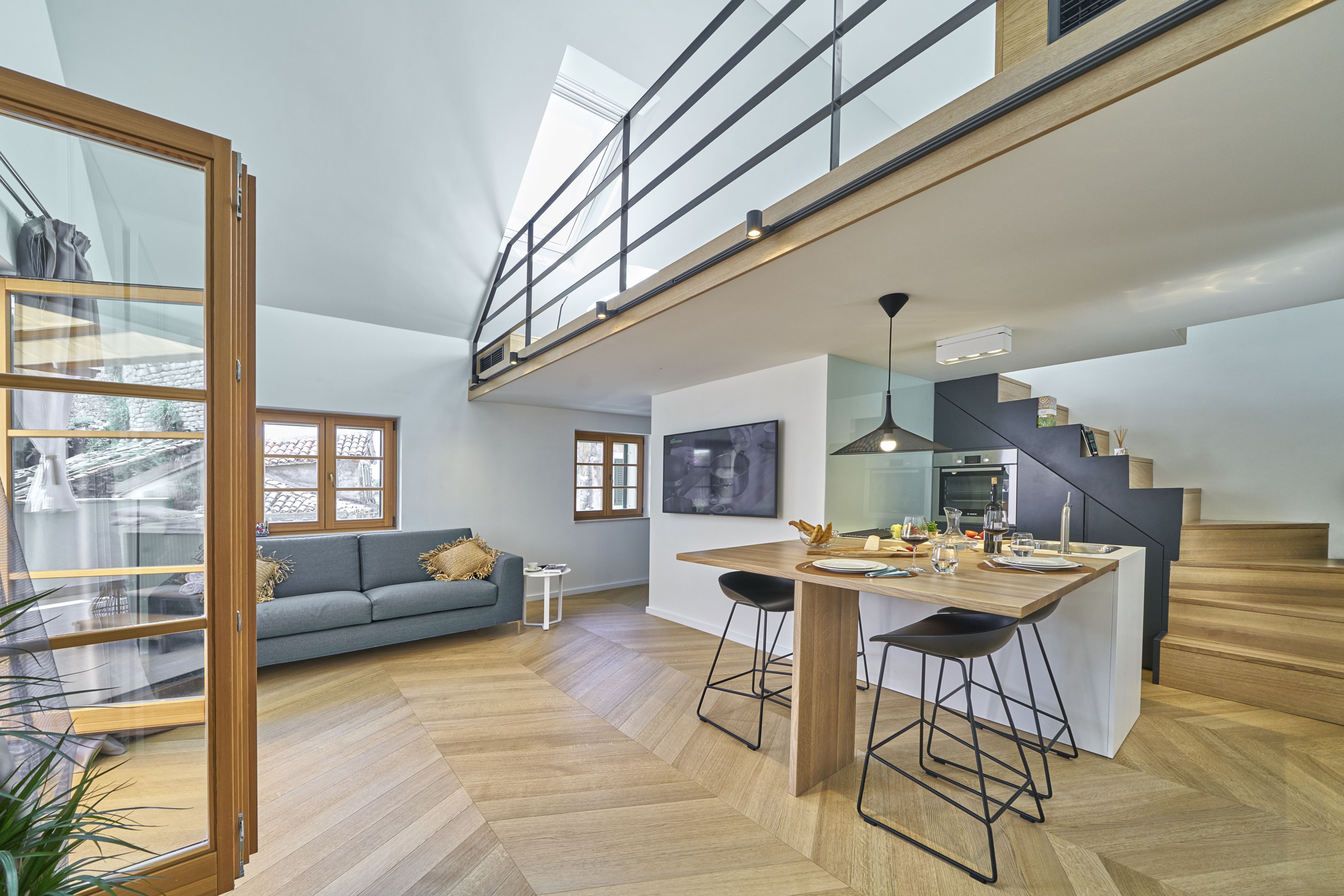 A spacious living area with a high ceiling, a staircase, and a kitchen area with a bar.