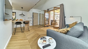 A modern living space with a kitchen area, a dining table with chairs, a grey sofa, and a coffee table with a book and remote control. - Villa Pergola (Sibenik)