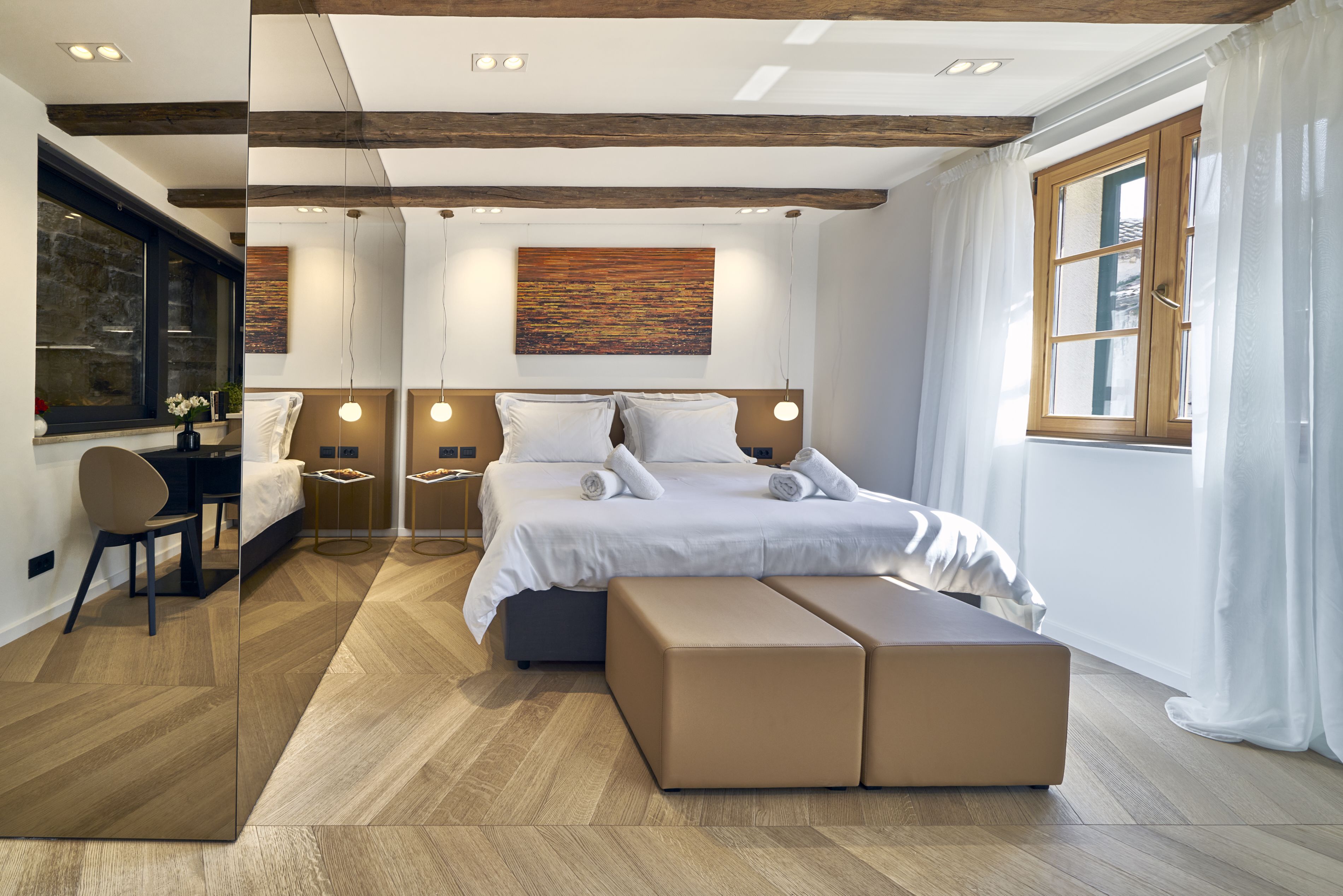 A modern bedroom with a large bed, bedside tables, a desk, and a window with curtains.