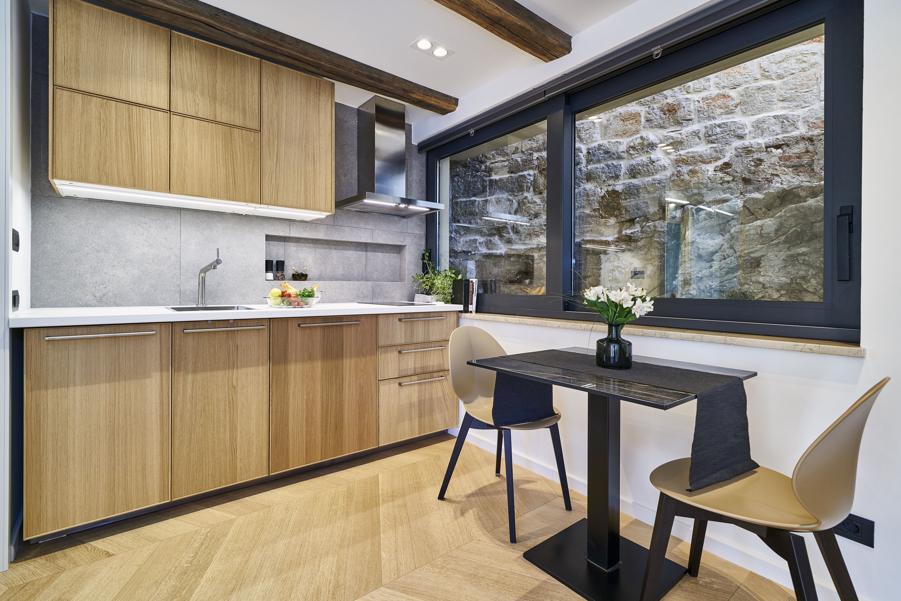 Una cocina moderna con armarios de madera, una pared de piedra y una ventana con vista a una construcción de piedra.
