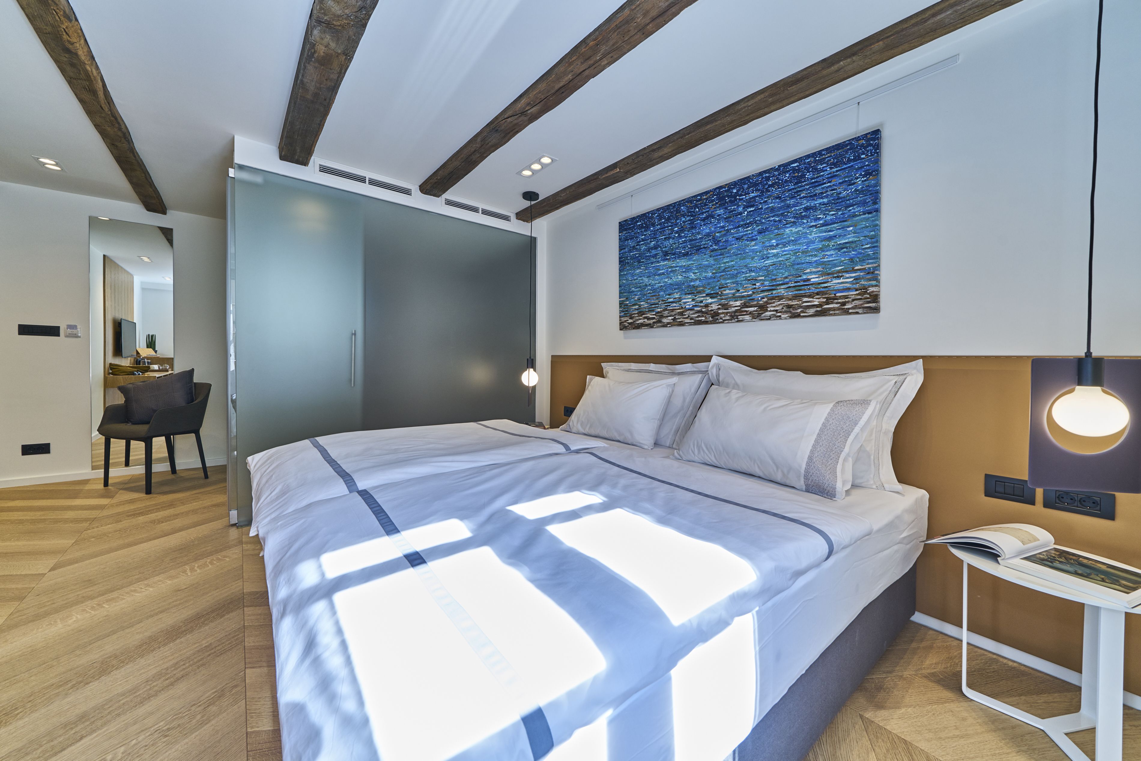 A modern bedroom with a large bed, a nightstand, a wall-mounted lamp, and a painting of a starry night.