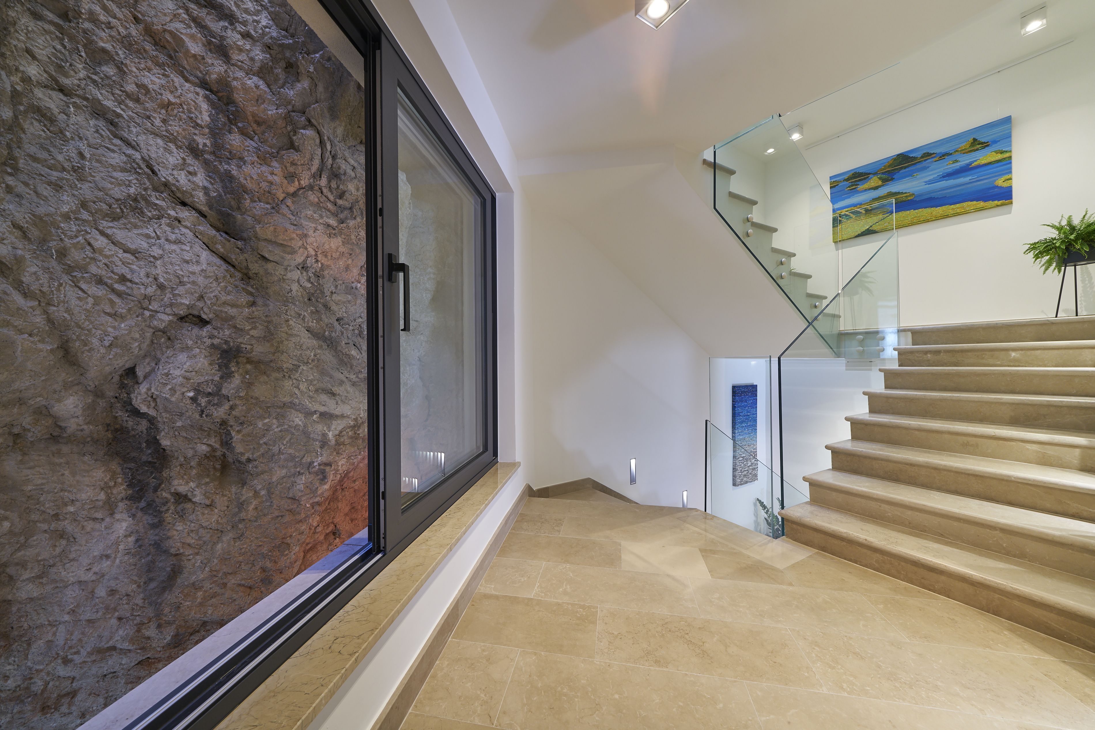 Un interior moderno con una pared de piedra, una escalera de cristal y un cuadro.