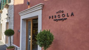 A building with a sign reading "villa PERCOLA" and a door with a glass panel. There are potted plants in front of the entrance. - Villa Pergola (Sibenik)