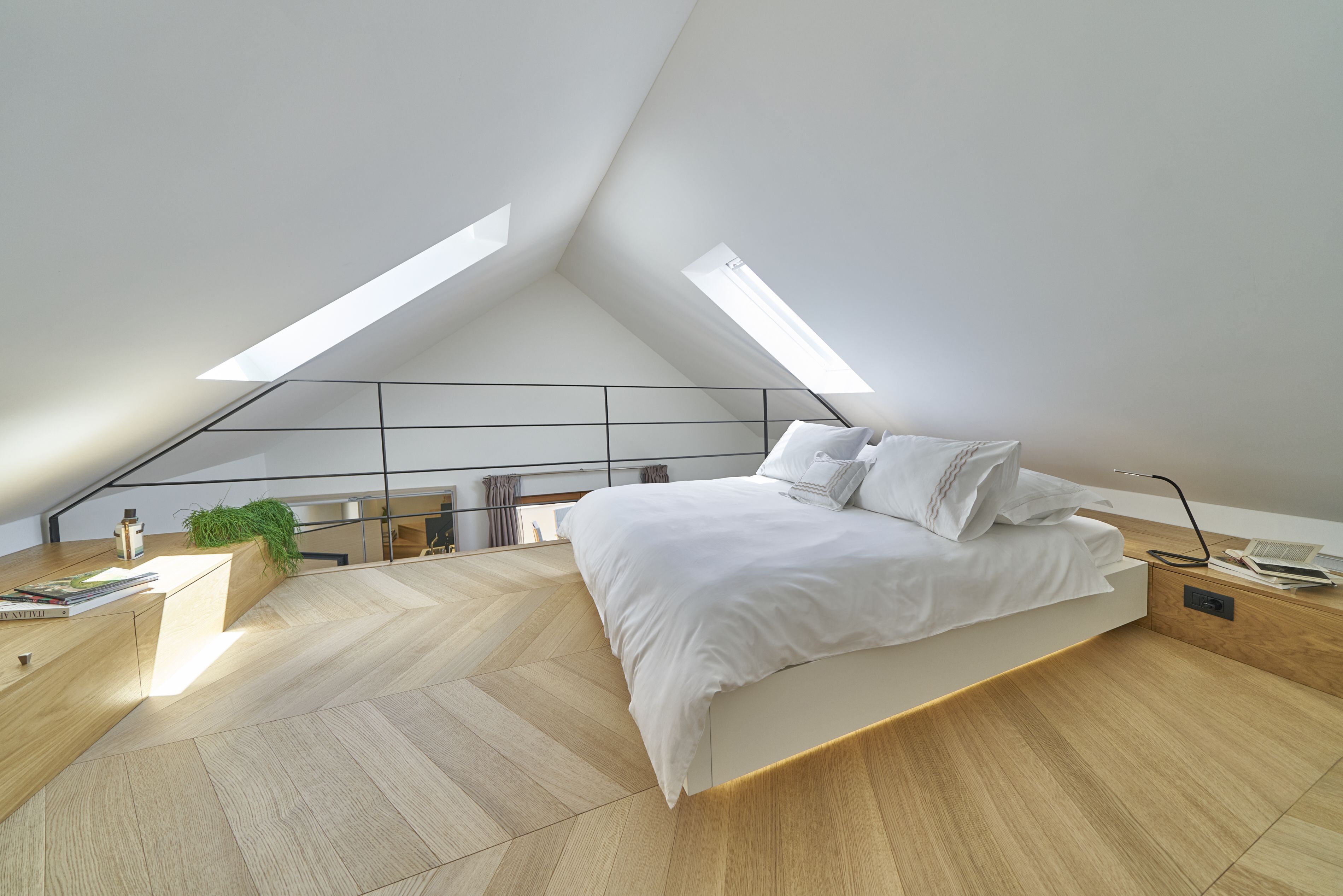 Une chambre moderne avec un plafond en pente, un lit avec une literie blanche, un bureau en bois et une petite plante.