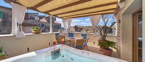 A hot tub with a table and chairs, surrounded by potted plants and a pergola.