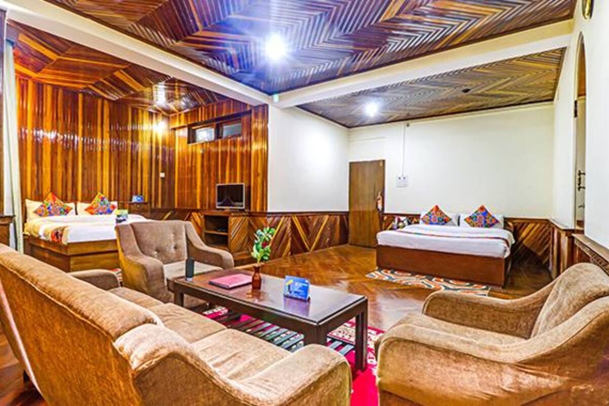 A hotel room with wooden paneling, two beds, a sofa set, a coffee table, and a television.