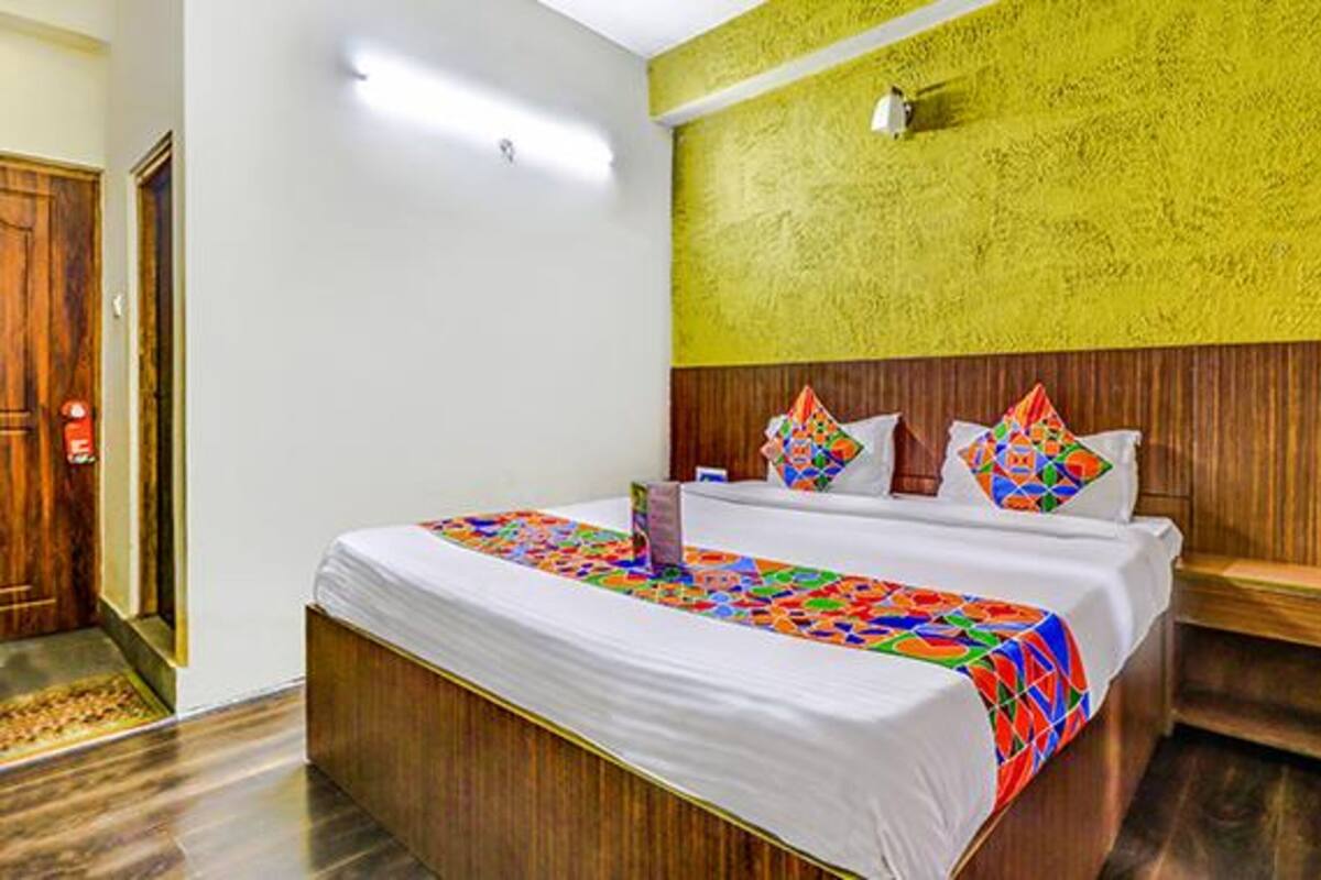 A hotel room with a wooden bed, a colorful quilt, a wooden headboard, and a yellow textured wall.