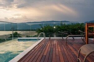 Eine Holzterrasse mit Pool und Liegestühlen mit Blick auf Strand und Berge.