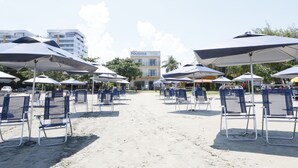 A beachside area with rows of beach chairs and umbrellas, a building with a sign reading "POUSADA", and a clear sky. - Pousada Conca di Mare (Bertioga)