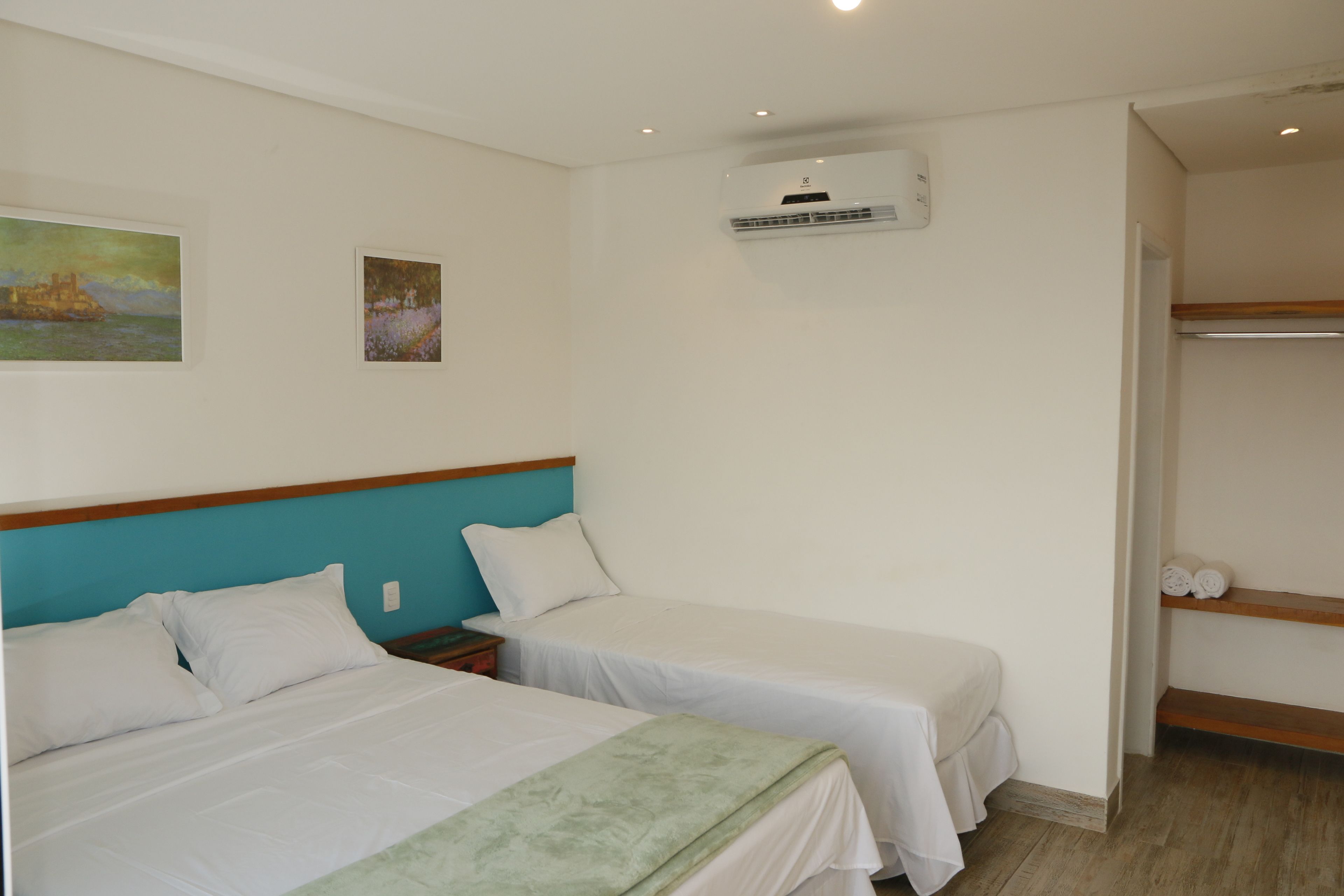 A hotel room with two single beds, a wooden headboard, a wall-mounted air conditioner, and a shelf with towels.