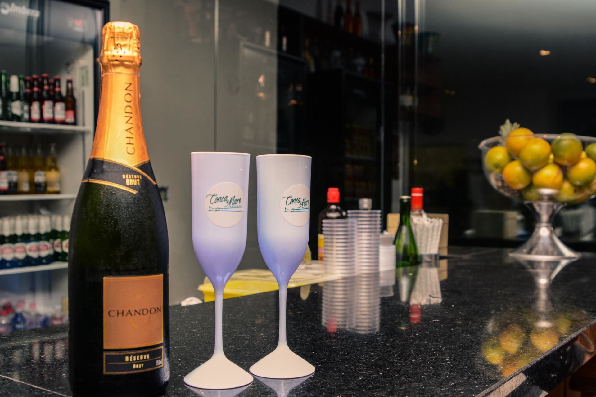 A bottle of Chandon champagne, two glasses, and a bowl of fruit on a bar counter.