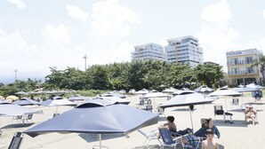 A beach with numerous umbrellas and lounge chairs, a building with a sign reading "POUSADA", and a clear sky. - Pousada Conca di Mare (Bertioga)