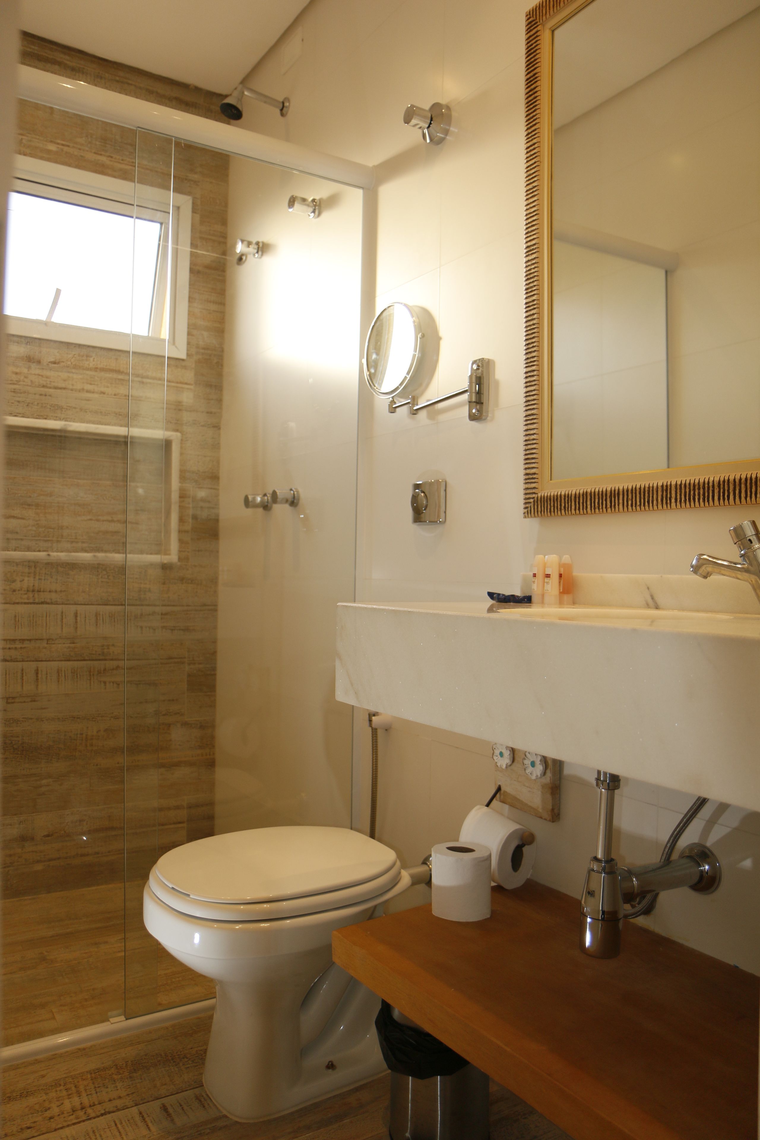 Un baño moderno con cabina de ducha de vidrio, inodoro, lavamanos con espejo y encimera de madera.