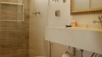 Un baño moderno con cabina de ducha de vidrio, inodoro, lavamanos con espejo y encimera de madera.