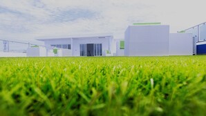 Un edificio moderno con techo plano, ventanas amplias y un primer plano con césped.