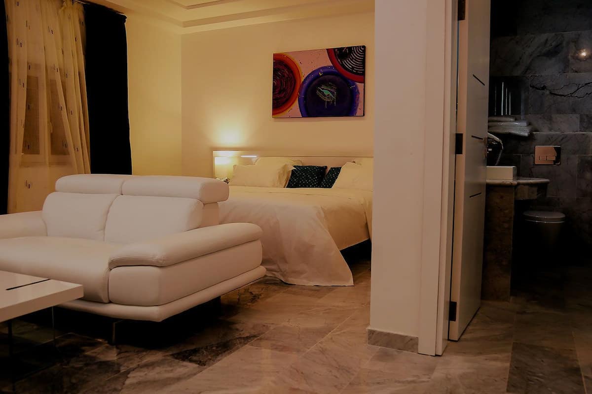 A hotel room with a bed, a sofa, a painting on the wall, and a bathroom visible through an open door.