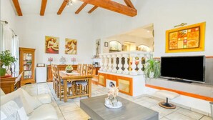 Amplia sala de estar con techo de madera, zona de comedor con mesa y sillas, televisor de pantalla plana en la pared y una estantería.