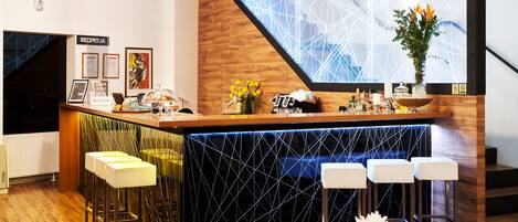 A modern bar area with a wooden counter, bar stools, and a large window with a geometric pattern.