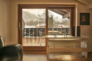 A room with a large sliding glass door leading to a balcony with a view of a snowy landscape and mountains.