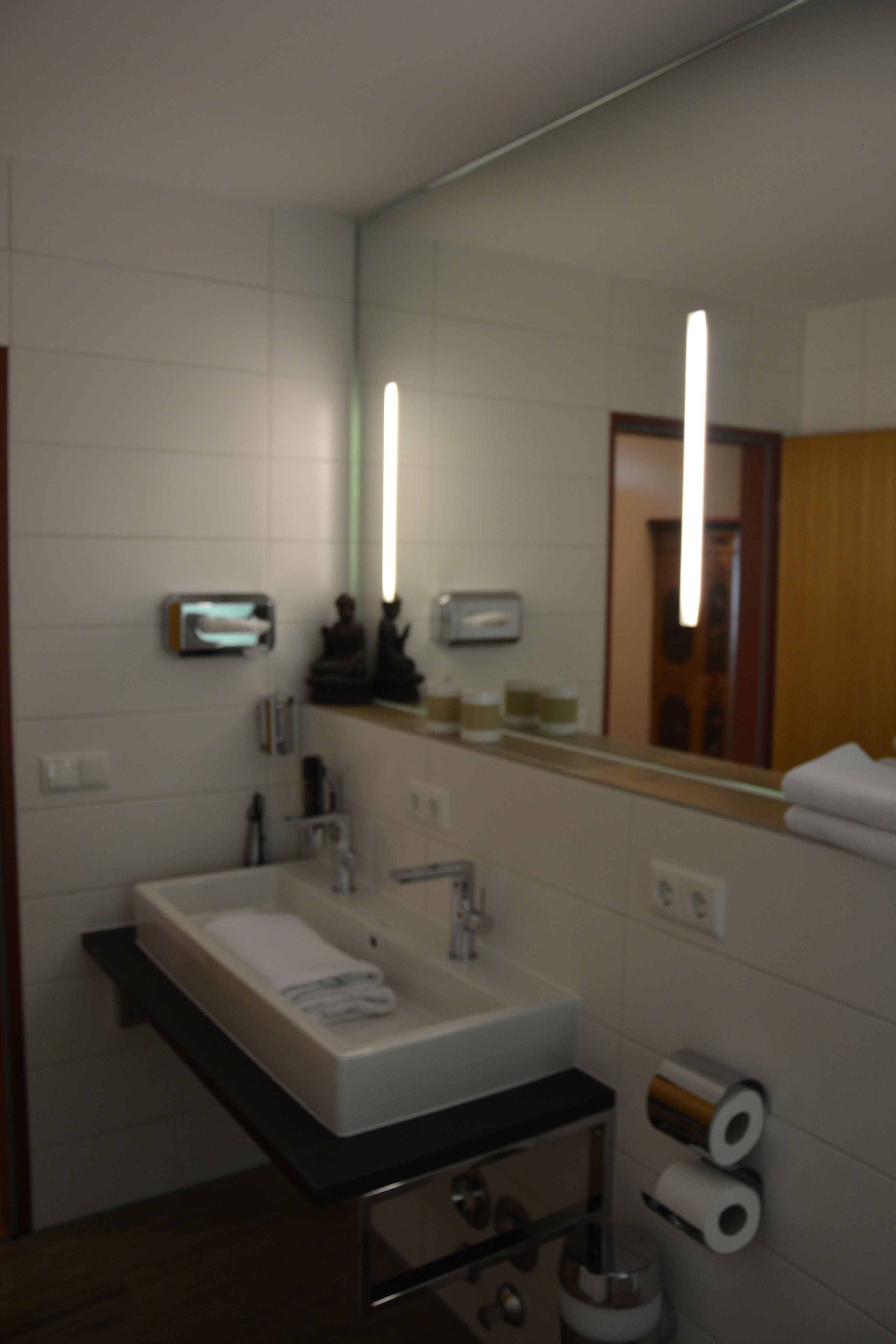 A bathroom with a sink, mirror, towel rack, and toilet paper.