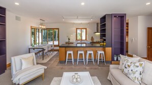 A modern kitchen with a central island, bar stools, and a dining area with a table and chairs.