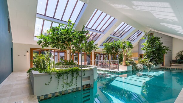 An indoor swimming pool with skylights, surrounded by greenery and modern architecture.