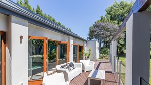 A modern outdoor patio with white furniture, glass doors, and a wooden deck.