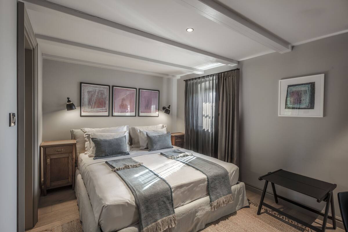 Une chambre à coucher comprenant un lit, des tables de chevet, un bureau et des œuvres d’art accrochées aux murs.