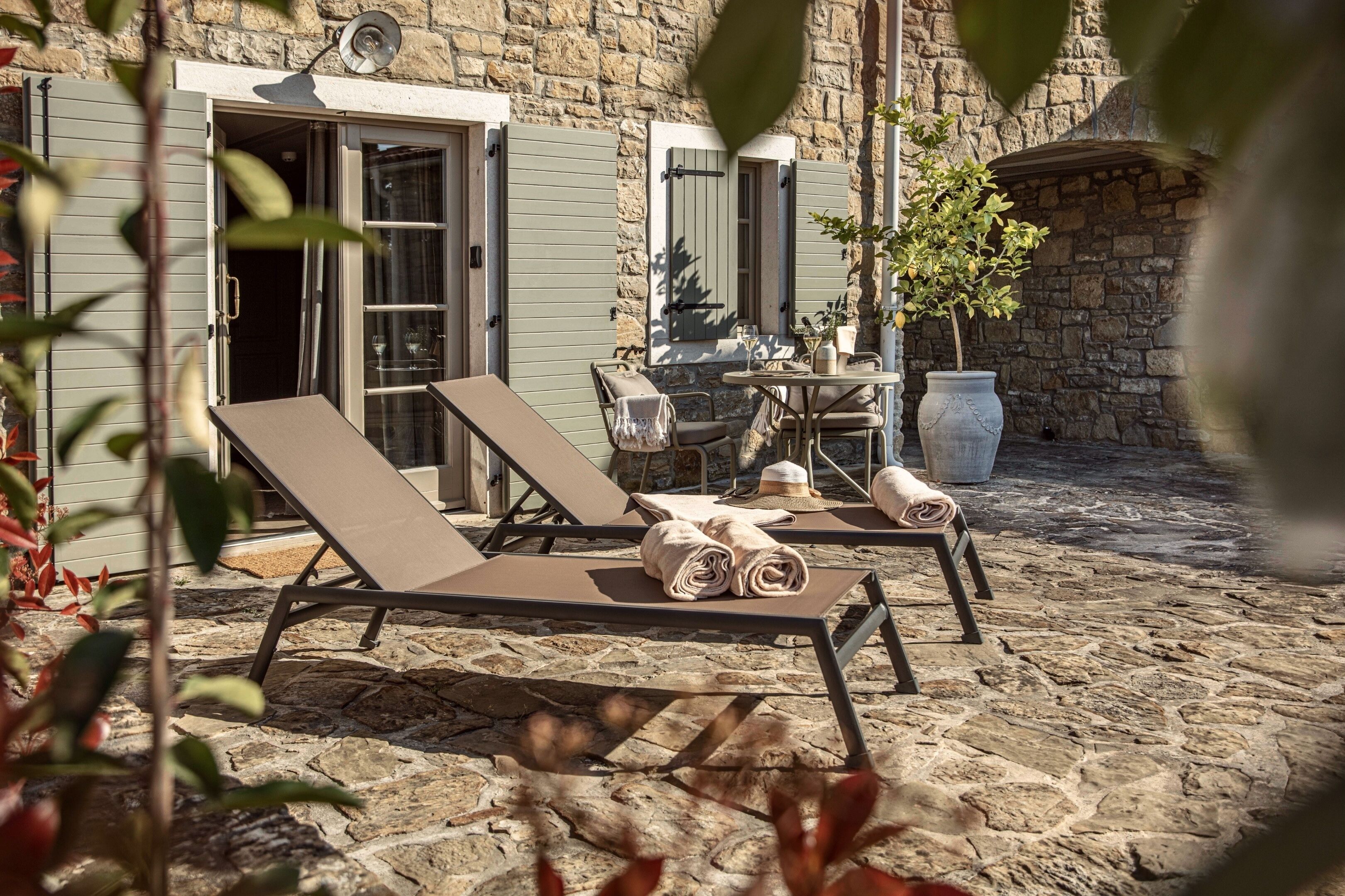 Eine Terrasse mit Steinboden, zwei Loungesesseln und einem Tisch, einem Blumentopf und einer Steinmauer.