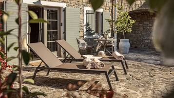 Eine Terrasse mit Steinboden, zwei Loungesesseln und einem Tisch, einem Blumentopf und einer Steinmauer.