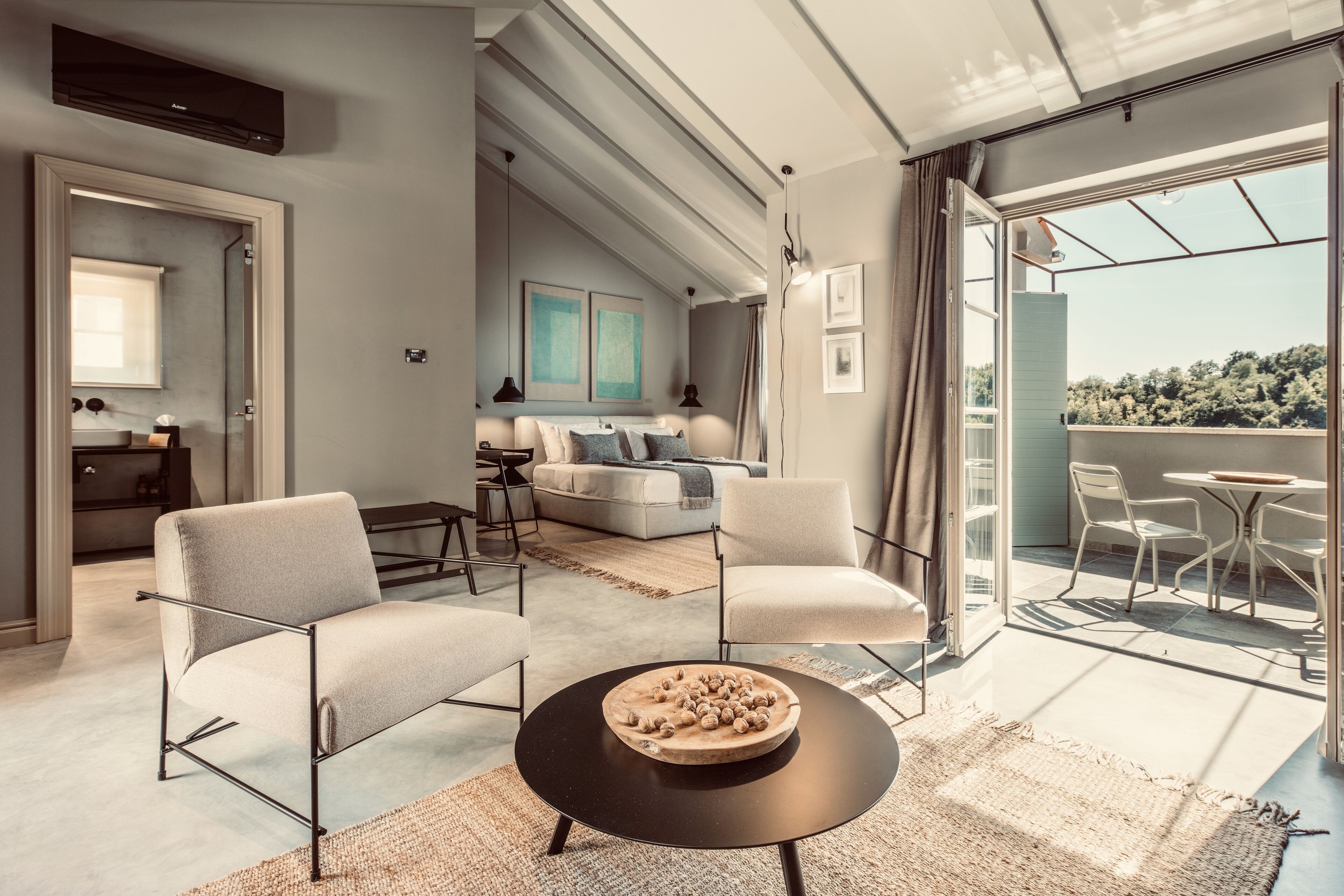 Una sala de estar moderna con un sofá, sillas, una mesa de centro y un balcón con mobiliario exterior.