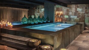 Un espace spa moderne doté d’un grand bain à remous rectangulaire, de murs en pierre et de bougies.