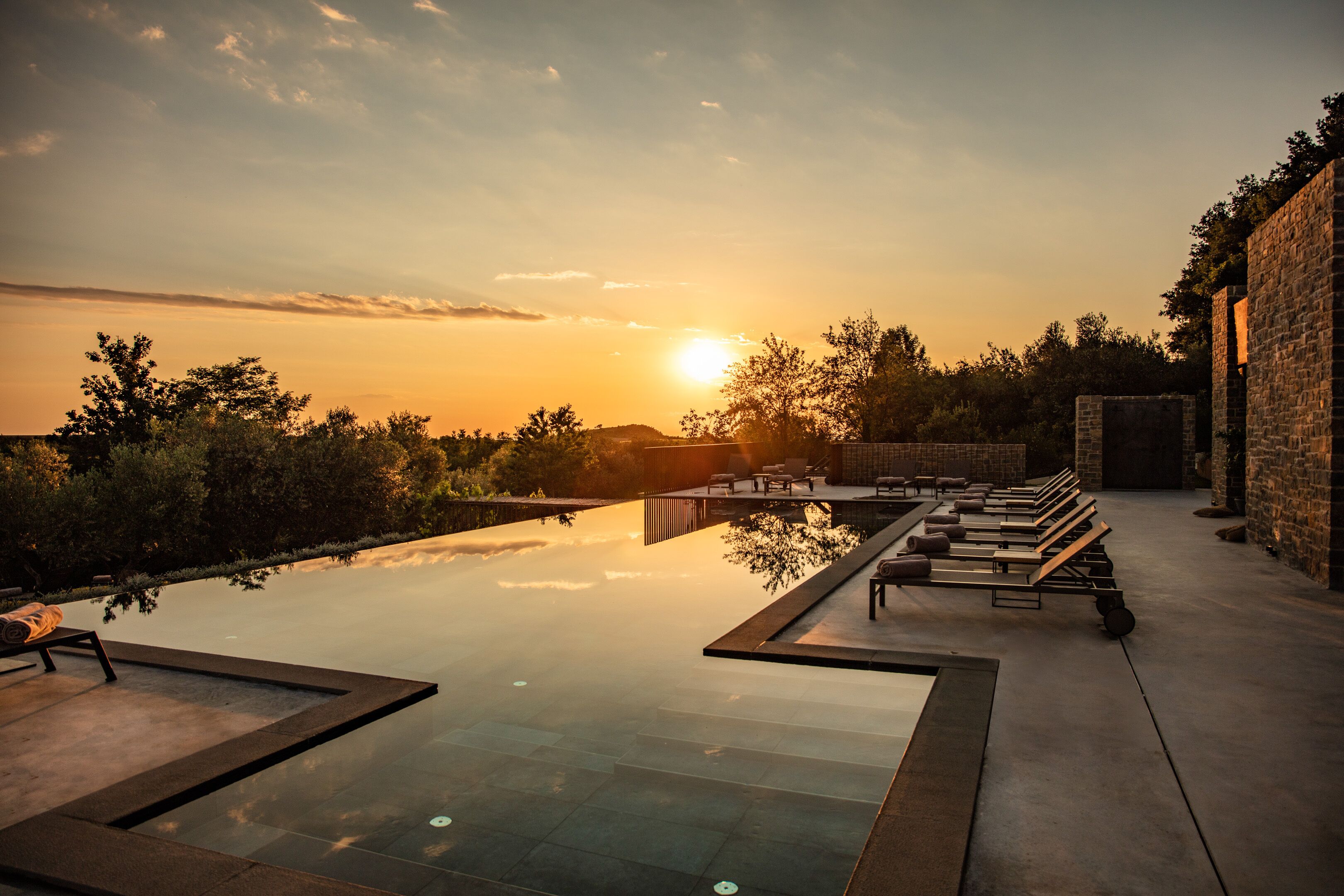 A rooftop infinity pool with lounge chairs and a sunset view.
