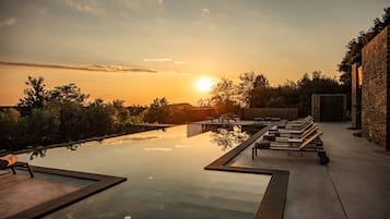 A rooftop infinity pool with lounge chairs and a sunset view.