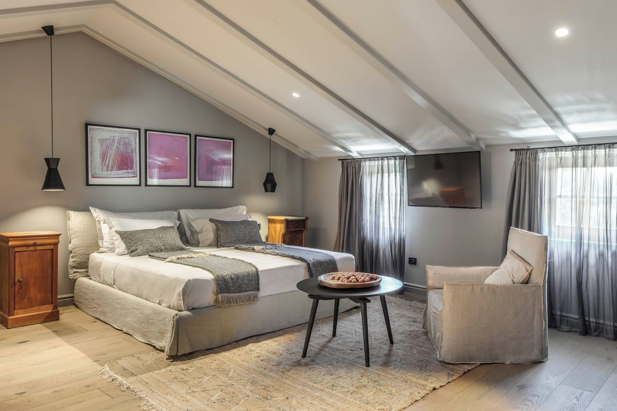 Une chambre avec un grand lit, une chaise, une petite table et un téléviseur fixé au mur.