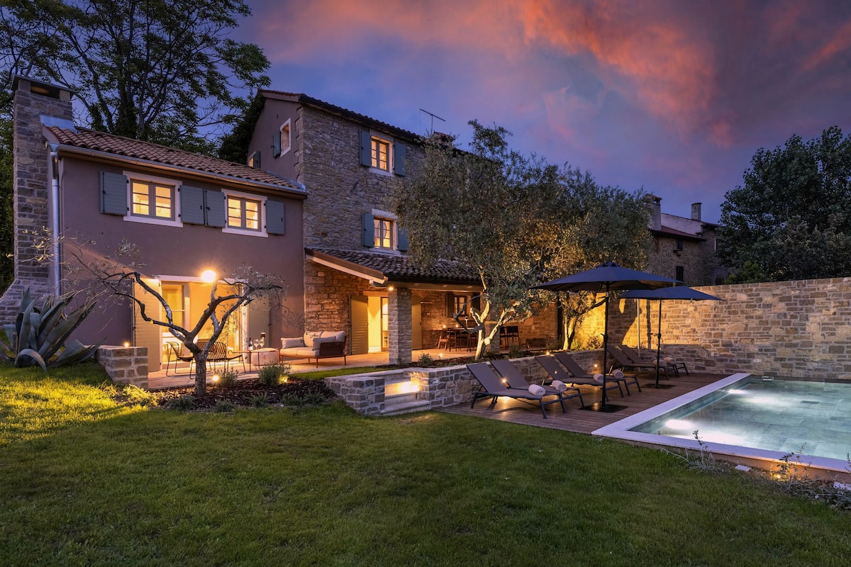 Une maison en pierre à deux étages, dotée d’une piscine, d’un espace salon extérieur et d’un patio.