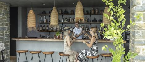A bar area with stools, a bartender, and shelves of bottles.