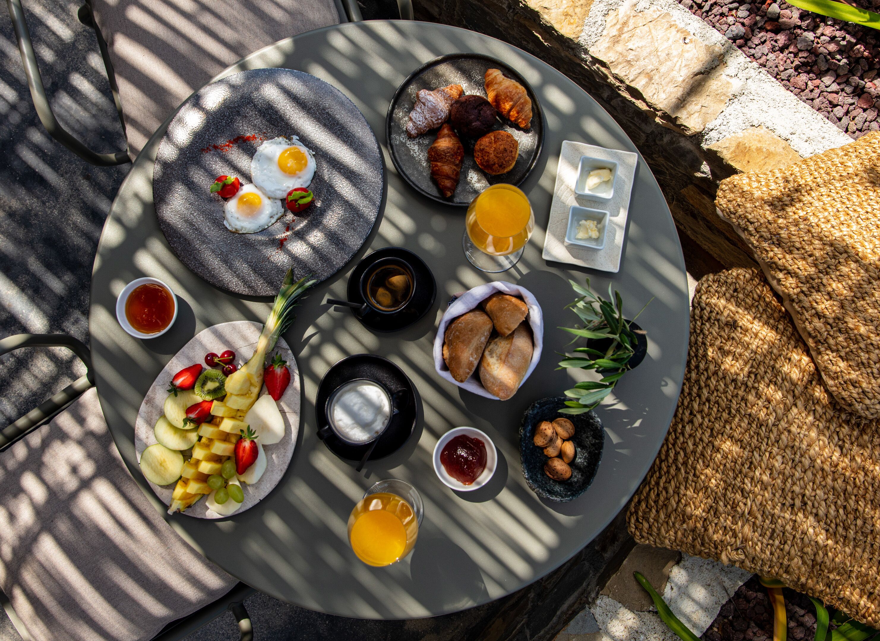 A round table with breakfast items including eggs, croissants, bread, fruit, and beverages.