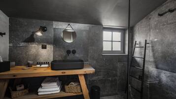 Un baño moderno con un mueble de tocador de madera, un espejo grande, un lavabo negro y una zona de ducha con puerta de cristal.
