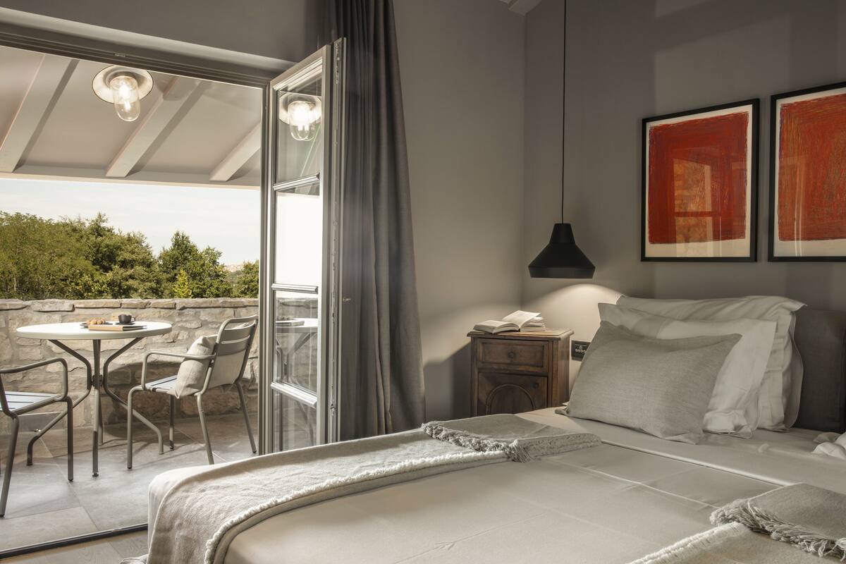 Une chambre à coucher avec un lit, une table de chevet, une lampe et une fenêtre donnant sur un espace verdoyant.