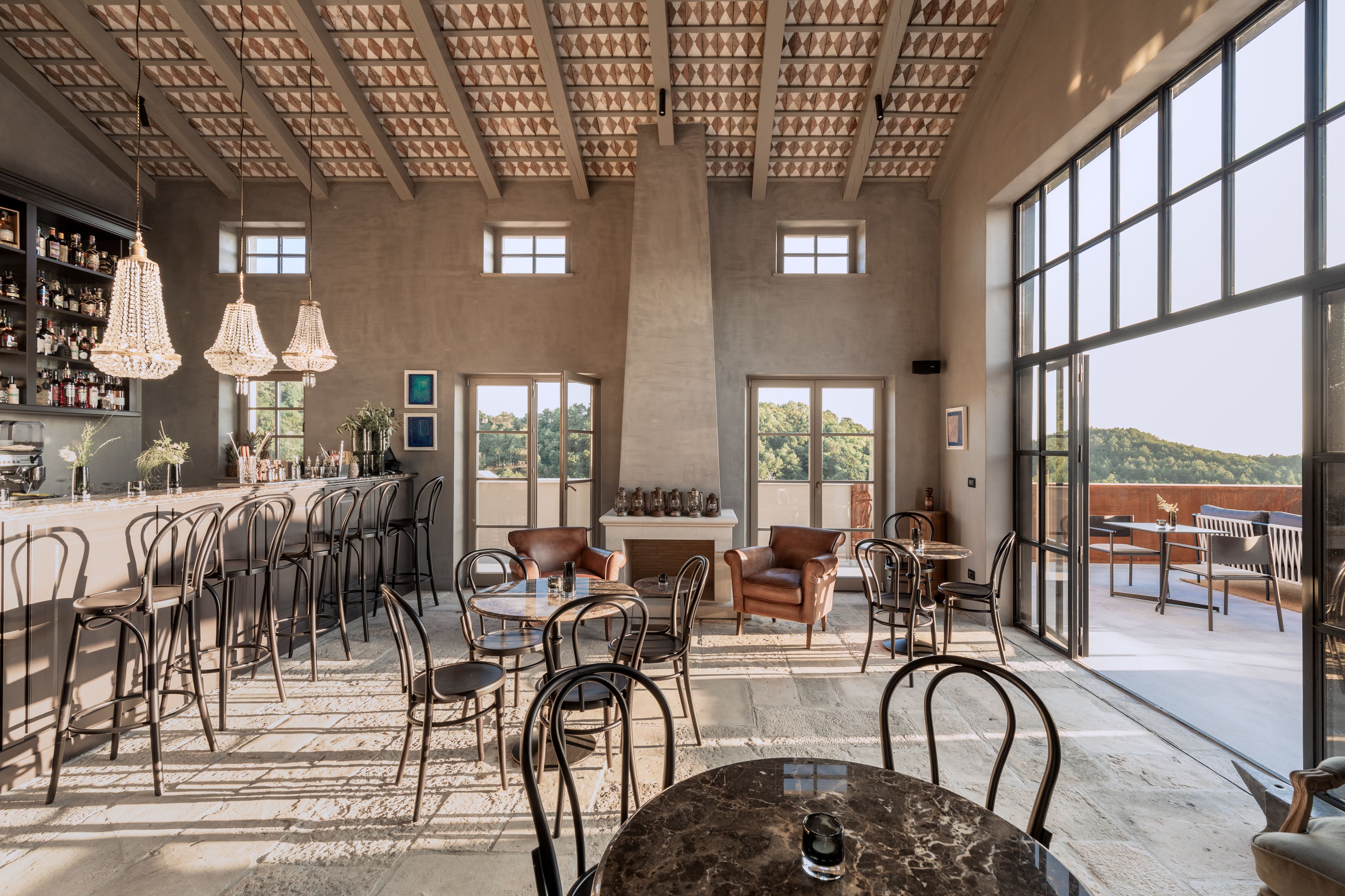 Un espacio interior amplio con techo alto, ventanas grandes y una zona de bar con estantes llenos de botellas.