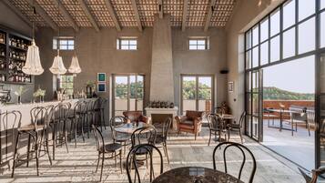 Un espacio interior amplio con techo alto, ventanas grandes y una zona de bar con estantes llenos de botellas.