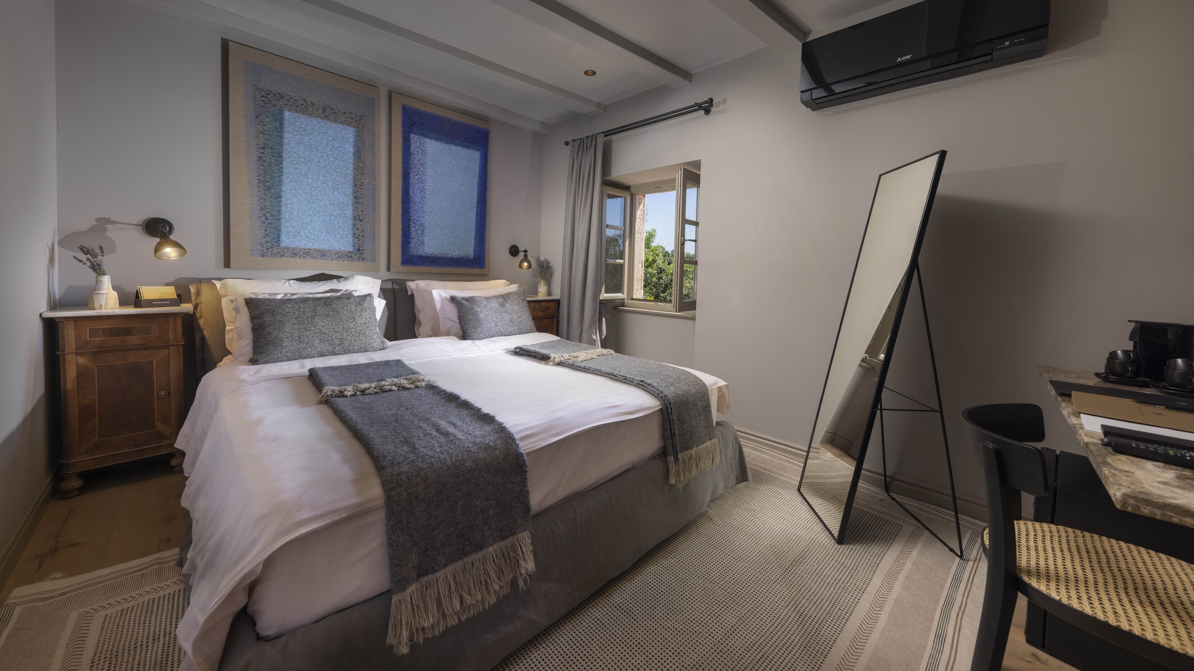 Una habitación de hotel moderna con una cama grande, un escritorio con computadora, un espejo y una ventana con cortinas.