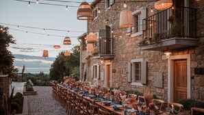 Un espace de restauration en plein air avec des murs en pierre, des guirlandes lumineuses et une longue table dressée pour un repas.
