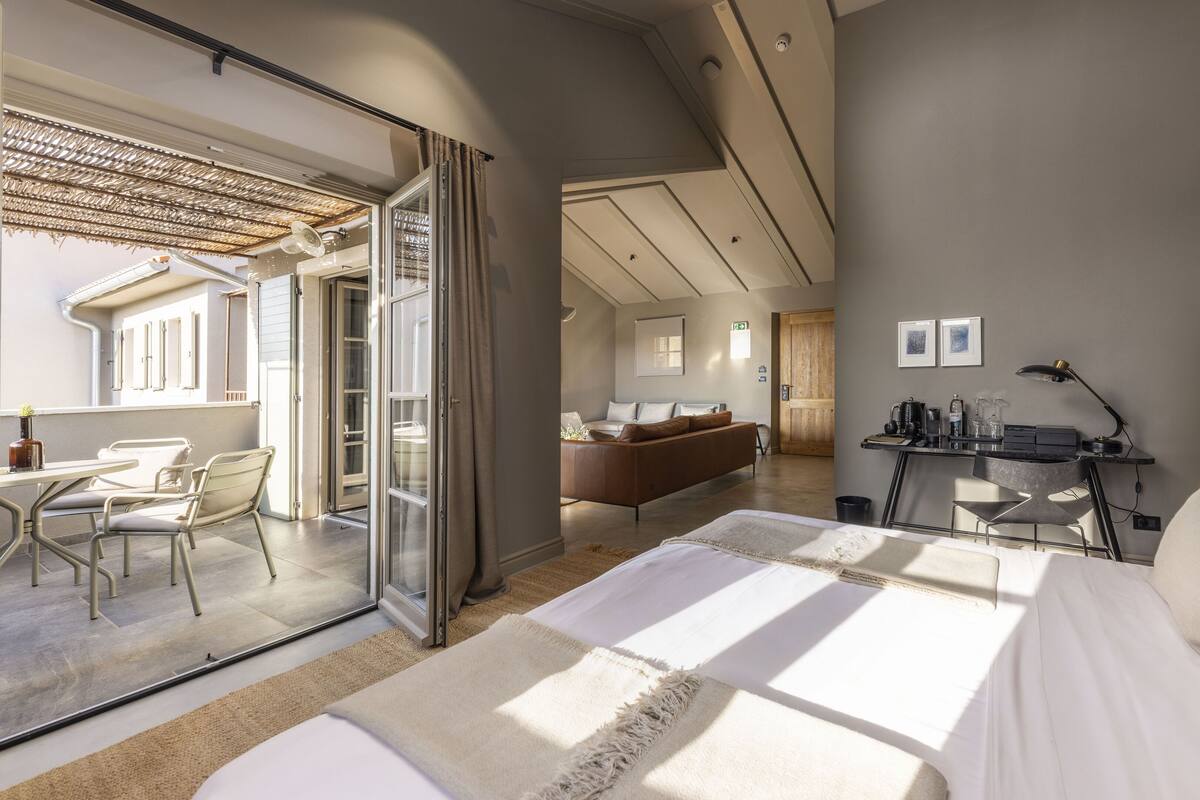 Une chambre d’hôtel moderne dotée d’un grand lit, d’un bureau avec une lampe, d’un canapé et d’un balcon avec une table et des chaises.