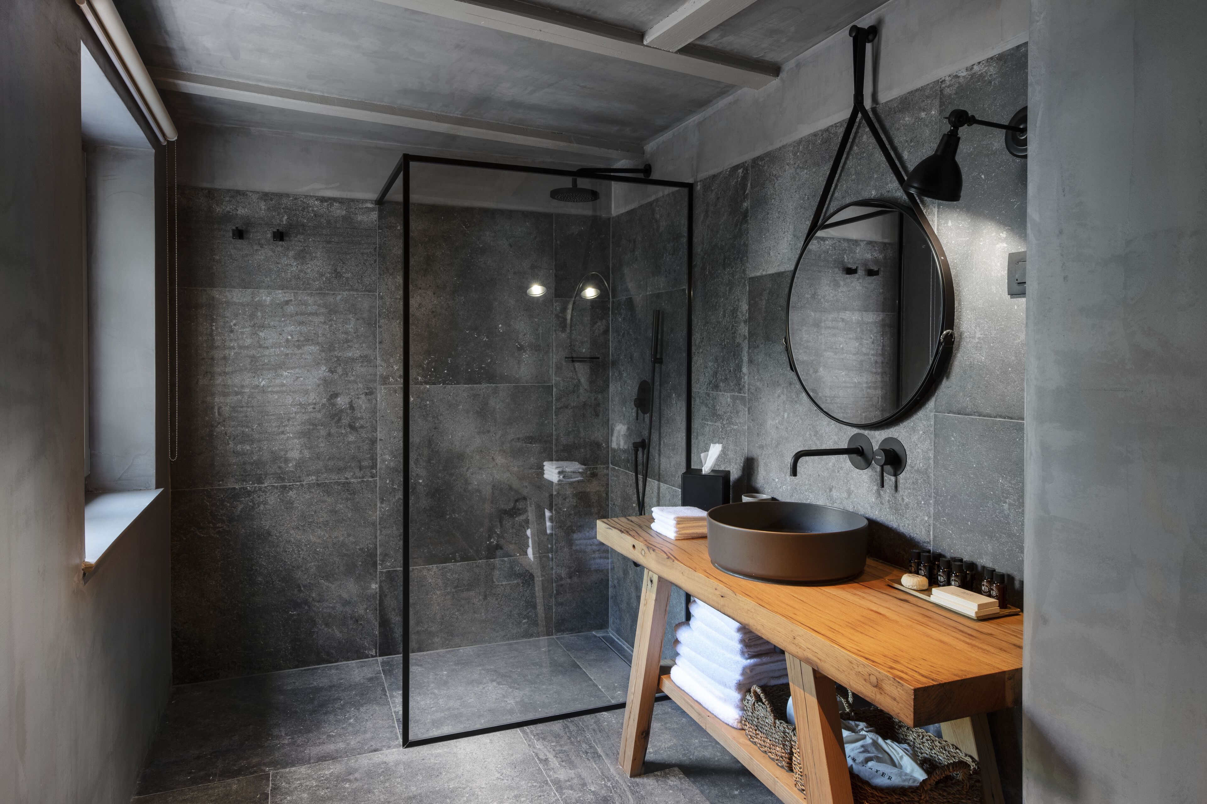 A modern bathroom with a glass-enclosed shower, a wooden vanity with a large basin, and a round mirror on the wall.