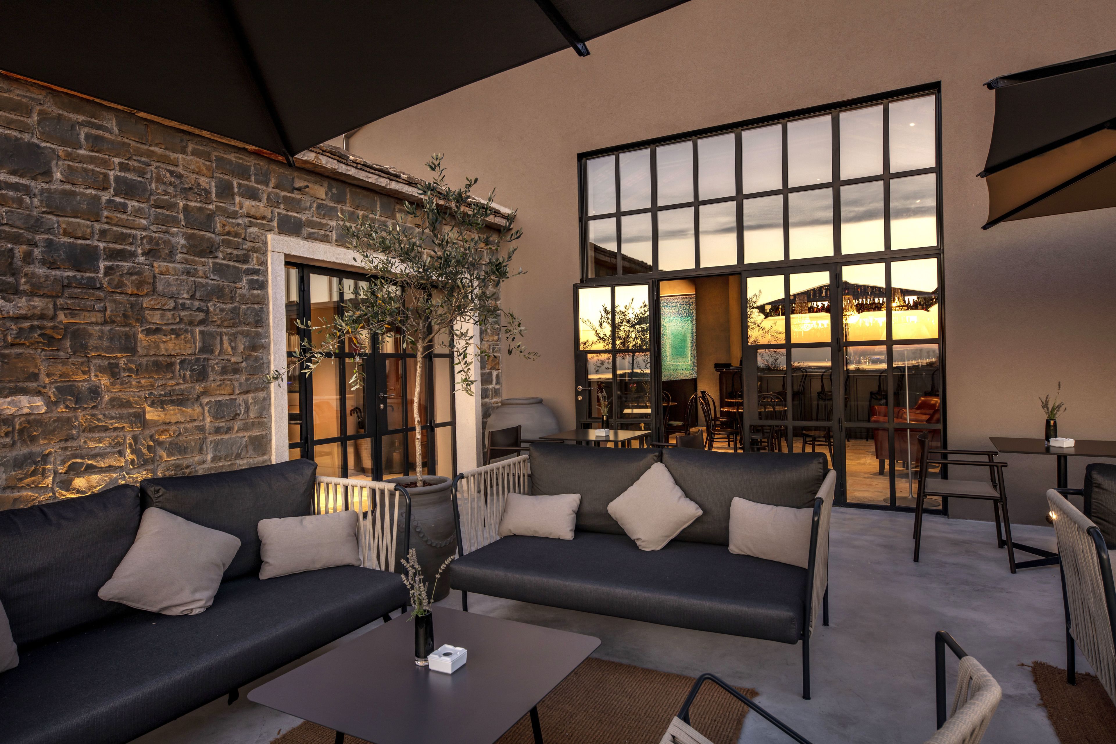 An outdoor seating area with stone walls, two sofas, a table, and a large window overlooking a building.