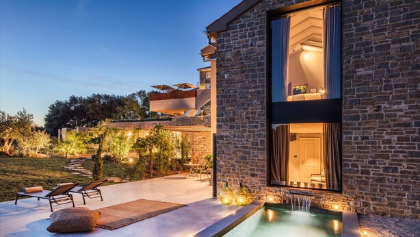 Une maison moderne dotée d’une piscine, d’un espace salon extérieur et d’une façade en pierre.